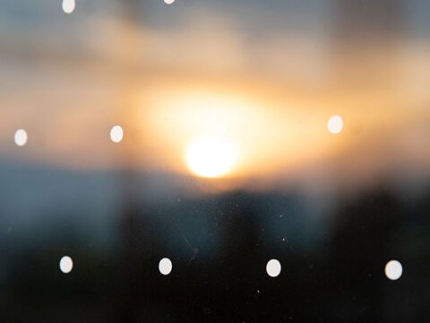 Dots on a window and burry reflection of sunset in the background.