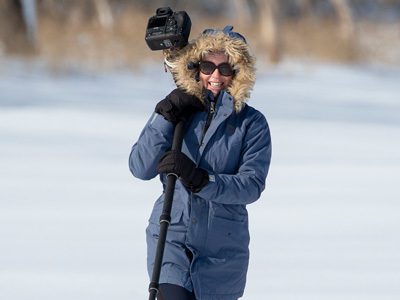 Woman standing on snow holding a long-lens camera.