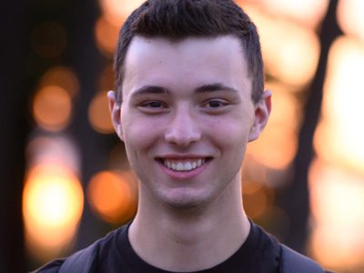 Young man smiling in front of a warm, blurred sunset background.