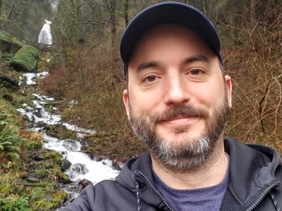 Man smiling in front of a forest stream