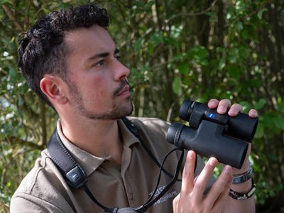 Man holding binoculars and looking to the side in a forest.