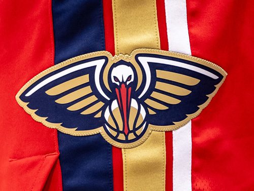 A close-up of a New Orleans Pelicans uniform patch featuring a stylized pelican with outstretched wings in navy, red, and gold.