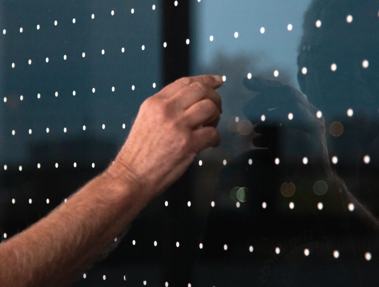 A hand touches one of the white dots on a window.