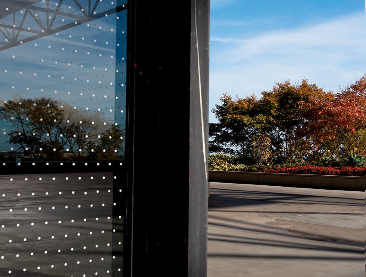 A corner of a building with white dots on its on its glass, showing how the dots break up the reflection.